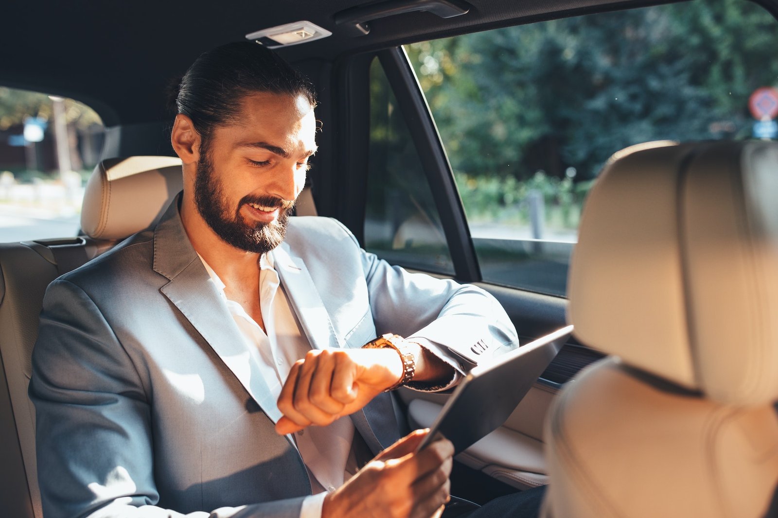 Businessman sitting in the back of a limousine, checking his watch while traveling in a comfortable and professional private hire vehicle.