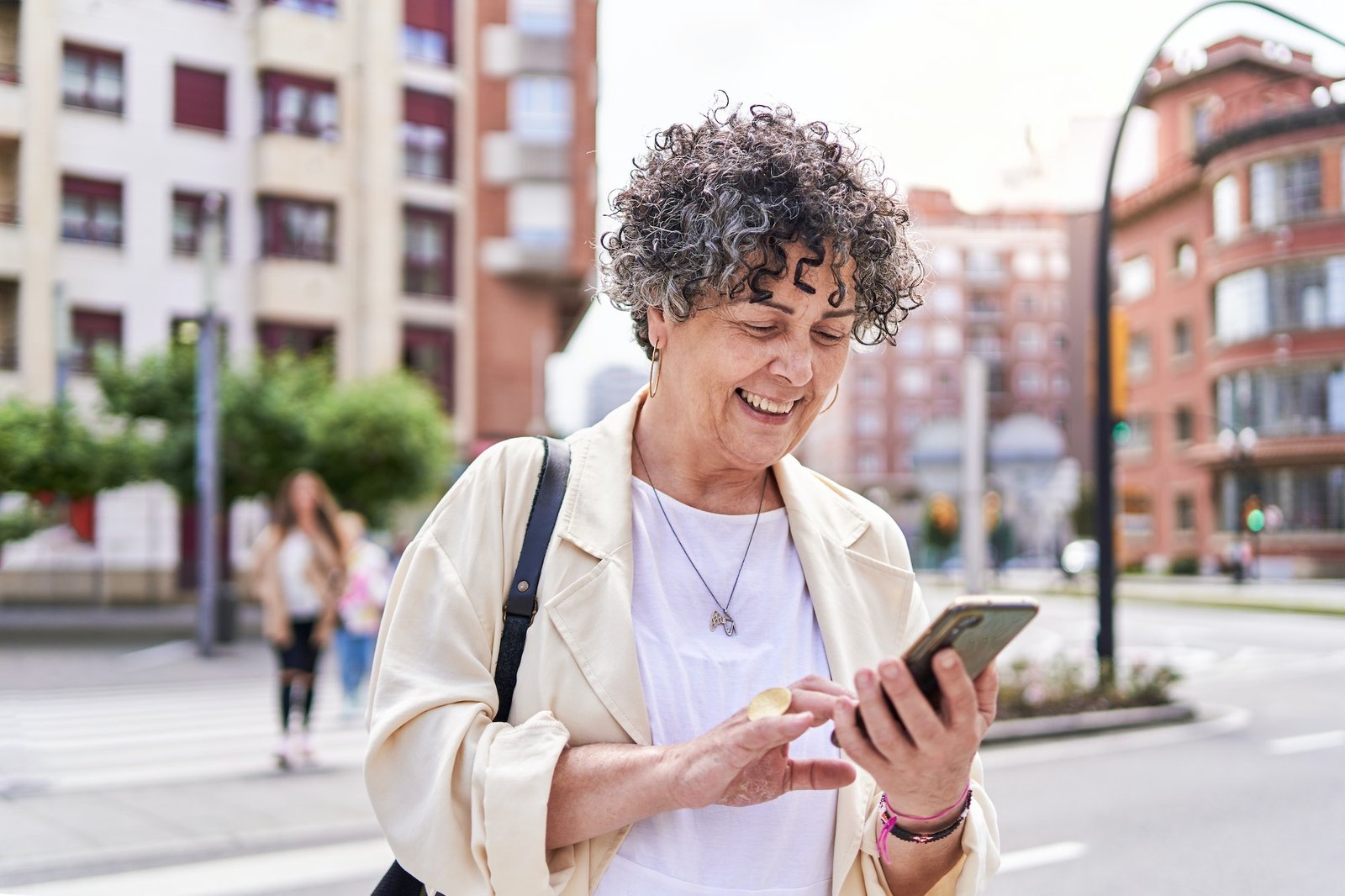 Mature woman using the Club Class Taxis app on her smartphone to book a taxi ride in a busy downtown city street.