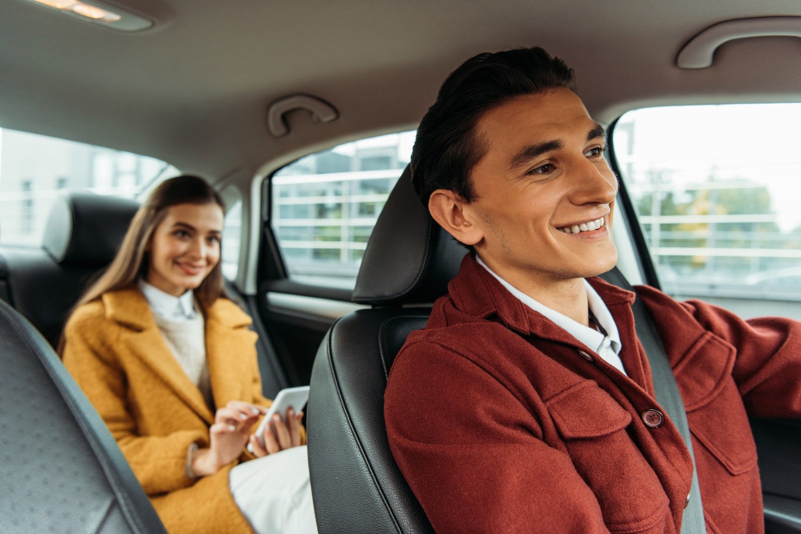 Smiling taxi driver interacting with a woman holding a smartphone inside a car, highlighting modern and customer-friendly taxi services.