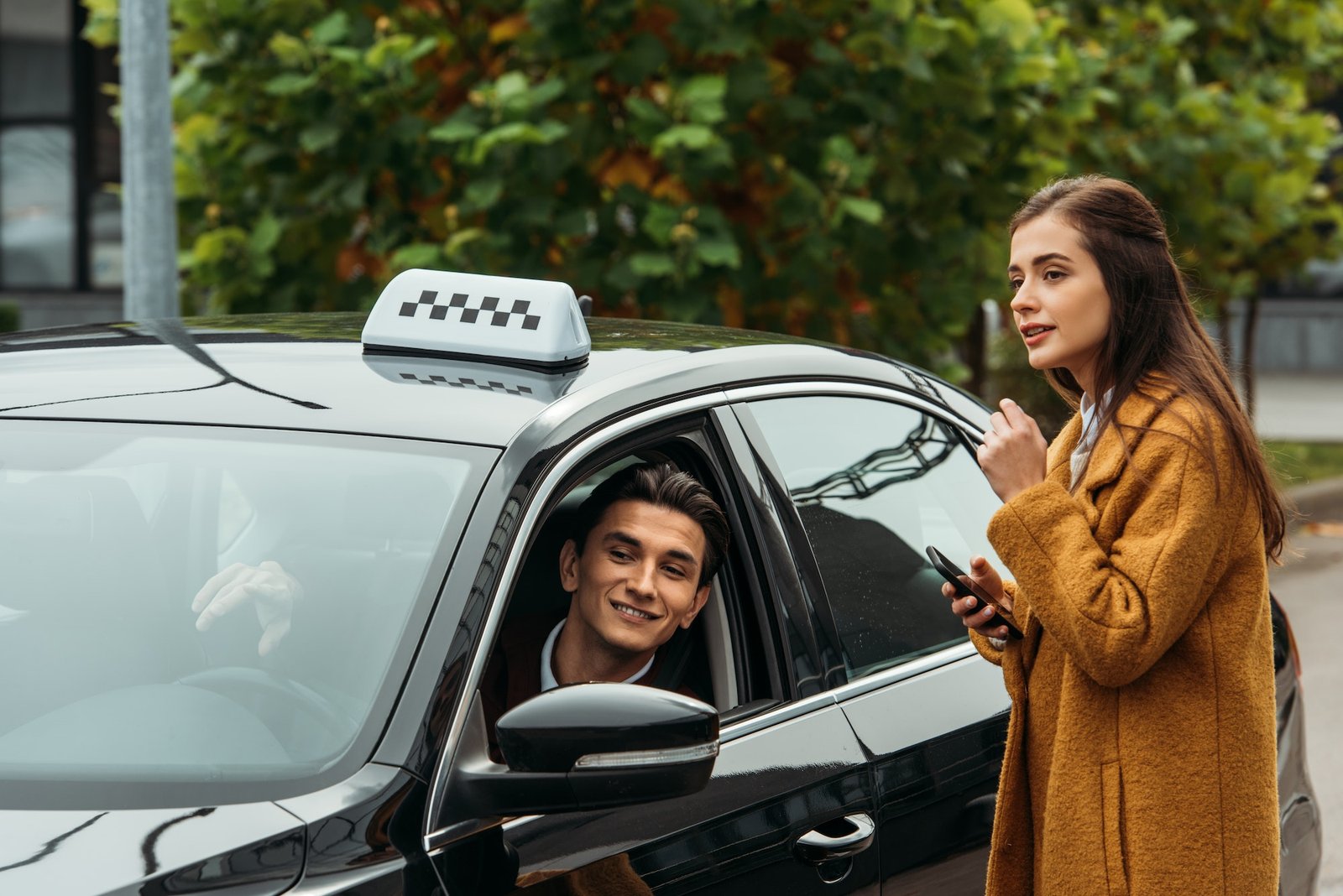 Young woman holding a smartphone and smiling while talking to a friendly taxi driver, representing a reliable and customer-focused Northwich taxi service.